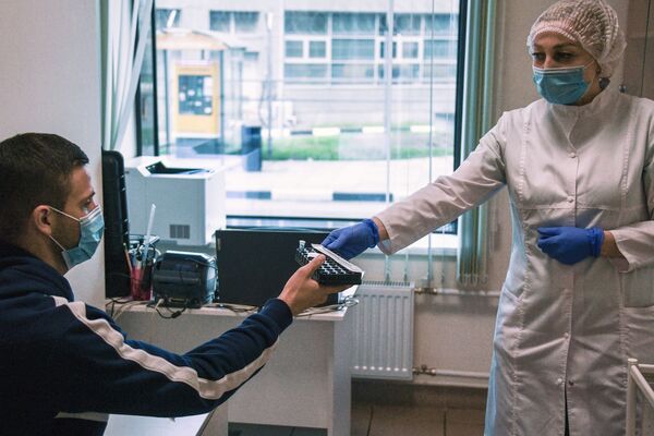 Сотрудник медицинской службы аэропорта Шереметьево проводит экспресс-тестирование пассажира на COVID-19 - Sputnik Латвия
