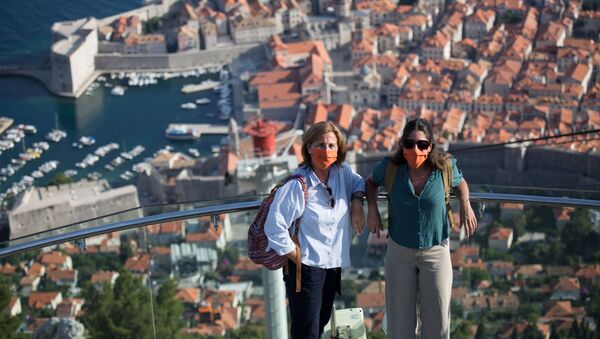 Tūristi aizsargmaskās pozē gaisa vagona augšējā stacijā virs Dubrovnikas vecpilsētas Horvātijā. - Sputnik Latvija