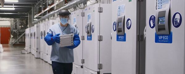 Сотрудник завода Pfizer возле холодильников с вакцинами от COVID-19 - Sputnik Latvija