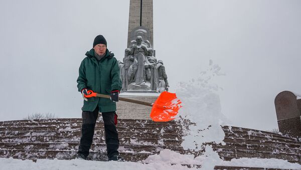 Мужчина убирает снег у памятника Свободы в Риге - Sputnik Латвия