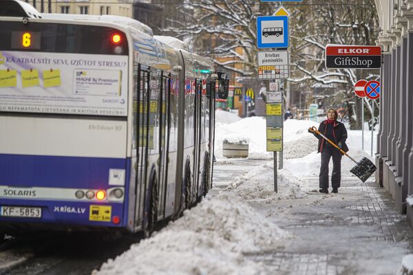 Женщина убирает снег на остановке общественного транспорта - Sputnik Латвия