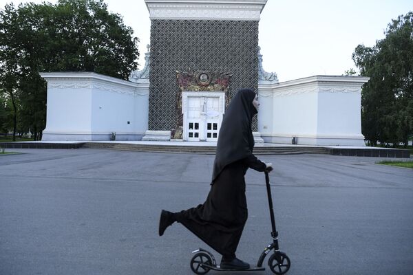 Женщина в хиджабе катается на скутере перед зданием с символикой Советского Союза во Всероссийском выставочном центре в Москве - Sputnik Latvija