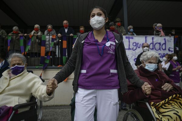 Медицинский работник в доме престарелых Сан-Херонимо в маске держит за руки двух пожилых женщин во время участия в мероприятиях в Международный женский день в Эстелле, Испания - Sputnik Латвия