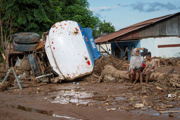 Люди сидят рядом с поврежденным грузовиком после внезапных наводнений, вызванных тропическим циклоном в индонезийской провинции Восточная Нуса - Тенгара - Sputnik Латвия