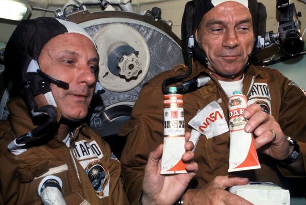 Amerikāņu astronauti Tomass Stafords un Donalds Kents Diks Sleitons ar padomju ēdiena tūbiņām Sojuz orbitālajā modulī. Konteineram ar boršču pielīmēta etiķete degvīns - Sputnik Latvija