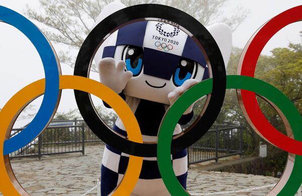 Талисман летней Олимпиады в Токио Miraitowa позирует сзади олимпийских колец после мероприятия по случаю 100 дней до Олимпийских игр в Токио  - Sputnik Латвия