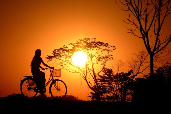 Индийская девушка катается на велосипеде во время заката в деревне Джойпур. - Sputnik Латвия