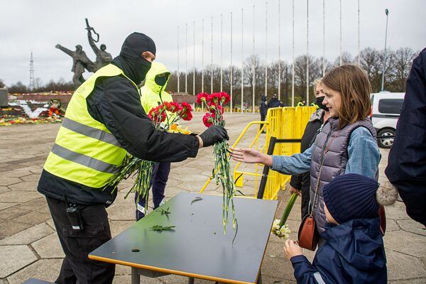 Люди оставляют цветы на столиках, после чего цветы относят к монументу - Sputnik Латвия