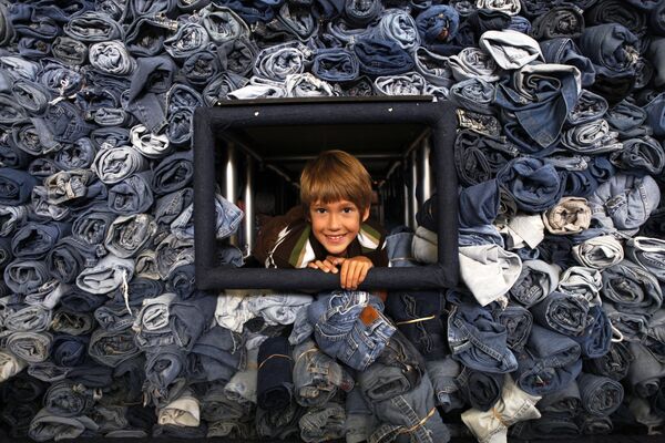 Zēns pabāzis galvu no vitrīnas ar 33 088 pāriem džinsu, ko savāca žurnāls National Geographic Kids pārstrādei par siltumizolācijas materiālu mājokļiem Vašingtonā, 2009. gads. Šis zēns savāca 1684 pārus - Sputnik Latvija