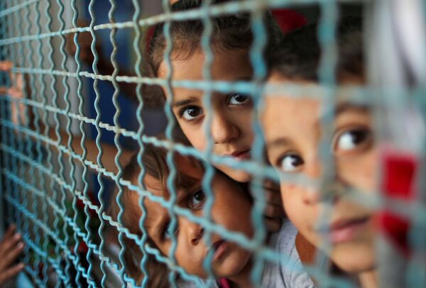 Палестинские дети, покинувшие свои дома из-за израильских воздушных и артиллерийских ударов, смотрят через оконное ограждение школы, управляемой Организацией Объединенных Наций, в которой они укрываются, в городе Газа, 18 мая 2021 года. - Sputnik Латвия