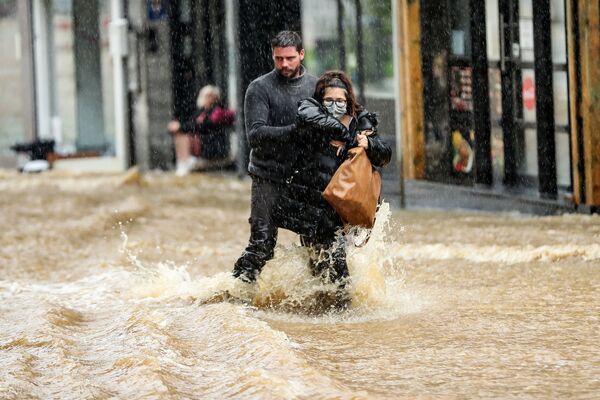 Мужчина помогает женщине пробираться по затопленной улице в бельгийском городе Спа. 14 июля 2021 года. - Sputnik Латвия