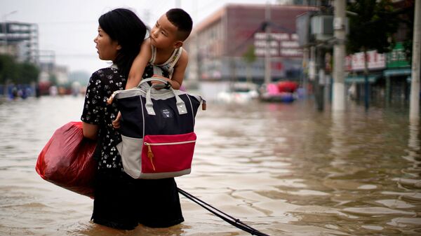 Женщина с ребенком и вещами пробирается через паводковые воды после проливного дождя в Чжэнчжоу, провинция Хэнань, Китай - Sputnik Latvija