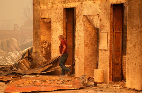 Житель осматривает сгоревшее коммерческое здание, принадлежащее его другу, после пожара, разразившегося в городе Гринвилл, штат Калифорния - Sputnik Латвия