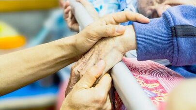 Социальный работник держит за руку пожилого человека