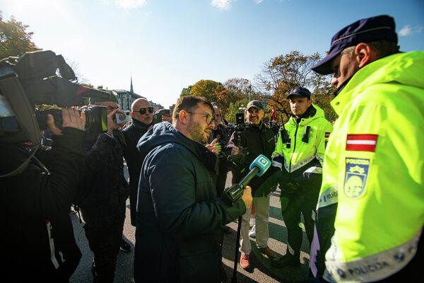 Latvijas televīzijas žurnālists Aleksejs Dunda lūdz policijas darbiniekus aizsargāt viņu un operatoru no uzmācīgiem protestētājiem - Sputnik Latvija
