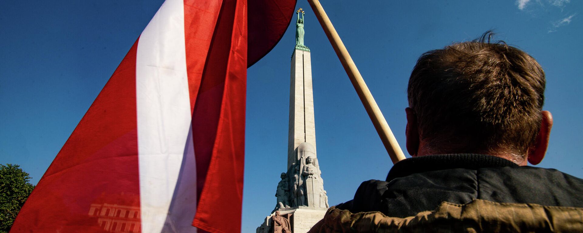 Мужчина с флагом Латвии у памятника Свободы в Риге - Sputnik Латвия, 1920, 12.03.2026