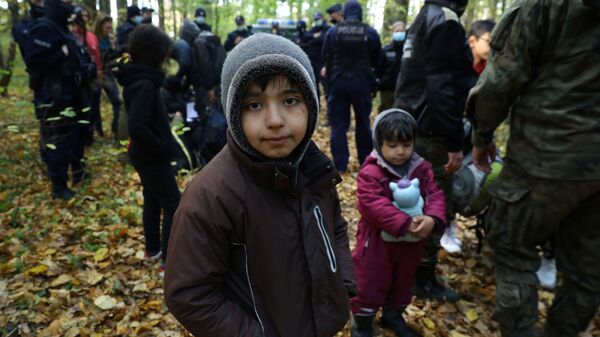 Иракский ребенок в окружении пограничников и полицейских после пересечения белорусско-польской границы в городе Хайнувка, Польша - Sputnik Латвия