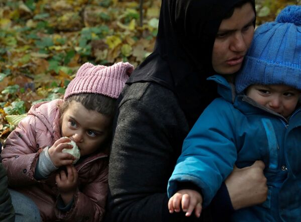Мигрантка из Ирака с детьми сидит в окружении пограничников и полицейских после пересечения белорусско-польской границы в городе Хайнувка, Польша. - Sputnik Латвия