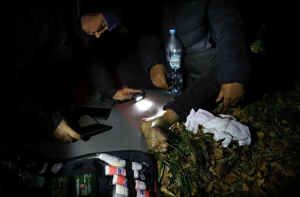 Сотрудник благотворительной организации осматривает рану мигранта, после того как тот пересек белорусско-польскую границу в лесу недалеко от Соколки, Польша. - Sputnik Латвия