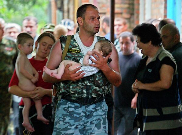 Šī fotogrāfija kļuvusi par Beslanas traģēdijas simbolu. Vēlāk mediji noskaidroja, ka bērnu no ieņemtās skolas zem teroristu automātiem iznesa milicijas leitnants no Ziemeļosetijas IeM Valsts ceļu satiksmes drošības inspekcijas operatīvās reaģēšanas vada Elbruss Gogičajevs - Sputnik Latvija