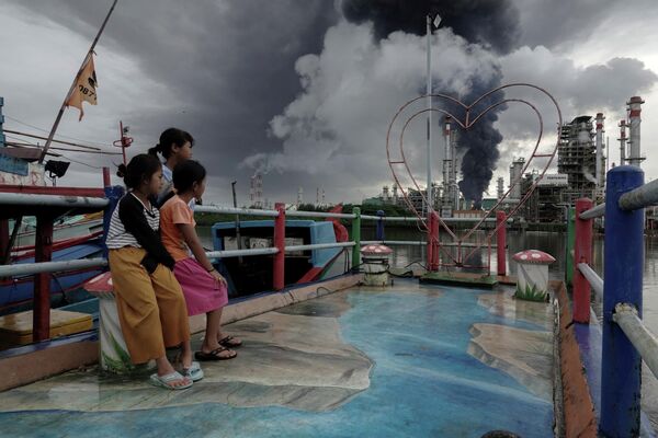Bērni vēro dūmus, kas paceļas naftas pārstrādes rūpnīcas ugunsgrēkā Indonēzijā - Sputnik Latvija