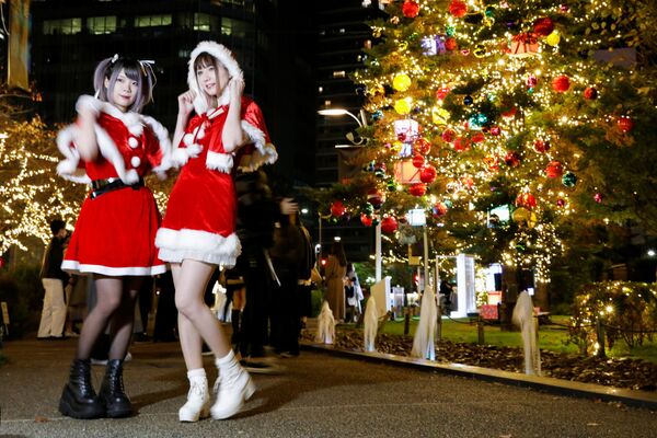 Девушки, одетые в костюмы Санта-Клауса, позируют на фоне рождественской иллюминации в Токио. - Sputnik Латвия