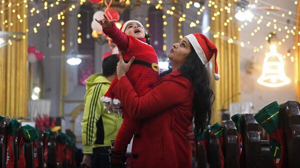 Мать держит ребенка в костюме Санта-Клауса накануне Рождества в церкви Святого Павла в Амритсаре, Индия - Sputnik Латвия