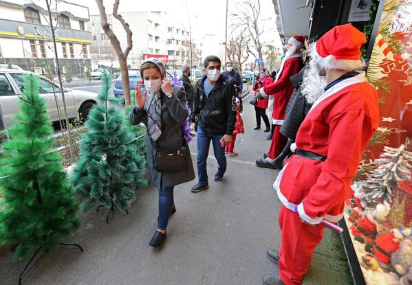 Мужчина в костюме Санты приветствует иранцев, проходящих мимо магазина рождественских украшений в Тегеране. - Sputnik Латвия