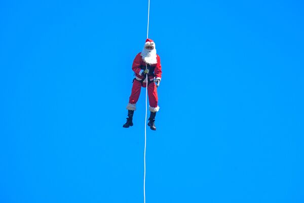Муниципальный пожарный Гектор Чакон в костюме Санта-Клауса спускается по канату с моста, чтобы доставить подарки детям в Гватемале. - Sputnik Латвия
