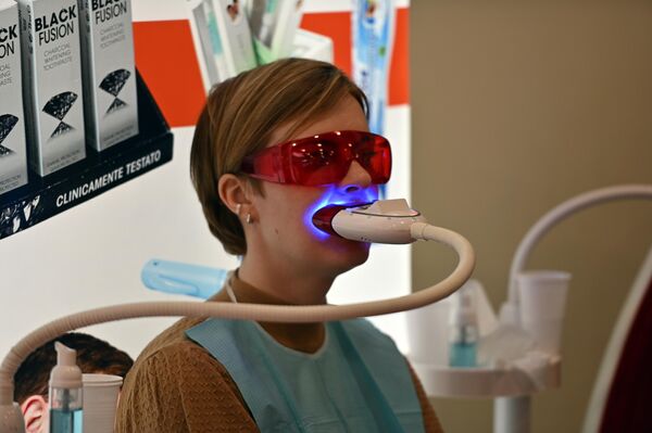 На фото: участница выставки на процедуре по отбеливанию зубов. - Sputnik Латвия