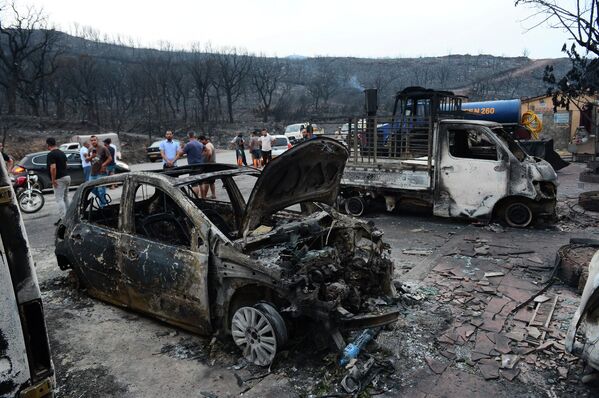 Люди осматривают сгоревшие автомобили после бушующих лесных пожаров в Буире, Алжир. - Sputnik Латвия