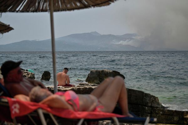 Люди загорают возле прибрежного города Саранда, когда клубы дыма поднимаются над греческим островом Корфу. - Sputnik Латвия