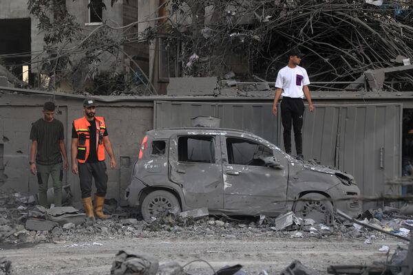 Спасатель и люди стоят около сгоревшей машины после удара со стороны Израиля в Рафахе на юге сектора Газа - Sputnik Латвия