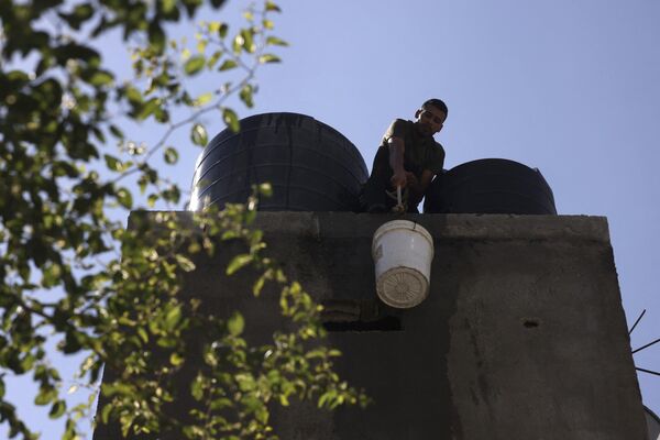 Мужчина поднимает ведро с водой, чтобы наполнить резервуар в лагере палестинских беженцев Рафах на юге сектора Газа - Sputnik Латвия