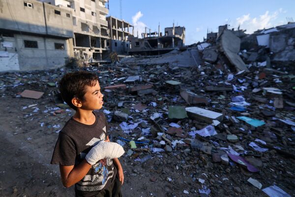 Раненый палестинский мальчик, 12-летний Мохаммед Софи, смотрит на разрушенное здание в лагере беженцев Рафах - Sputnik Латвия