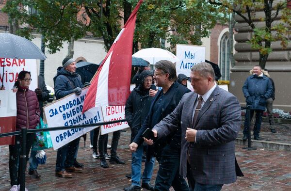 Лидер партии &quot;Латвия на первом месте&quot; Айнарс Шлесерс проходит мимо митингующих у здания Сейма Латвии - Sputnik Латвия