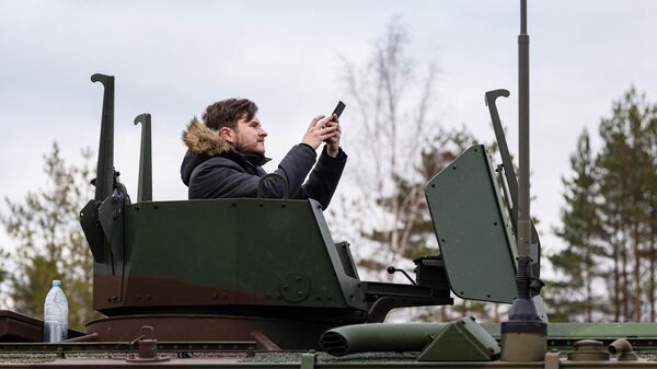 Один из участников экскурсии на военный полигон в Адажи позирует для селфи в бронетранспортере Patria 6х6  - Sputnik Латвия