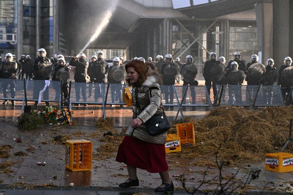 Женщина идет по заваленной навозом и сеном площади мимо полицейского оцепления во время акции протеста фермеров в Брюсселе. - Sputnik Латвия