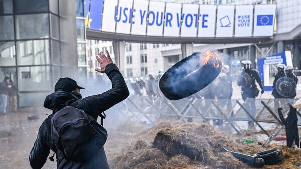 Протестующий бросает горящую покрышку в полицейских во время акции протеста фермеров в Брюсселе  - Sputnik Латвия