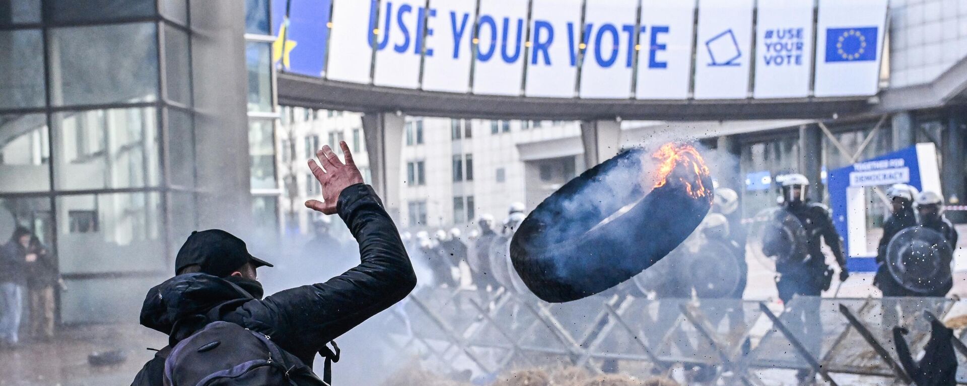Протестующий бросает горящую покрышку в полицейских во время акции протеста фермеров в Брюсселе  - Sputnik Латвия, 1920, 01.02.2024