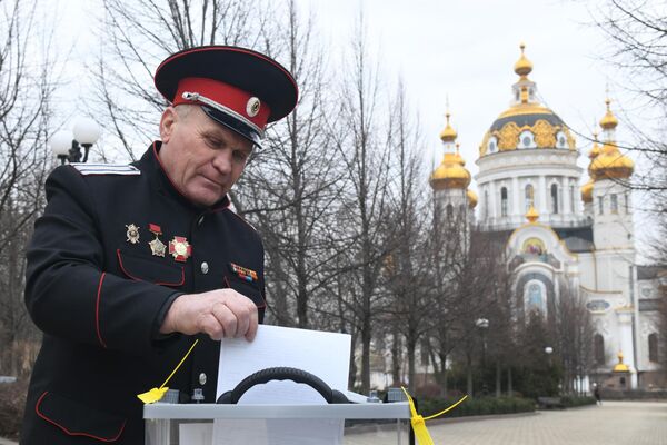 Мужчина опускает в урну бюллетень в ходе выездного голосования на выборах президента РФ в Донецке. - Sputnik Латвия