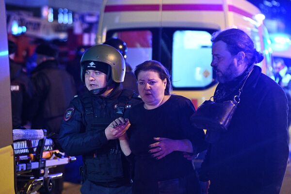 Сотрудник полиции оказывает помощь пострадавшим у концертного зала Крокус Сити Холл в Москве, где произошла стрельба - Sputnik Латвия