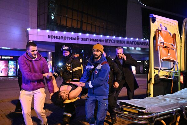 Сотрудники скорой помощи оказывают помощь пострадавшей у концертного зала Крокус Сити Холл в Москве, где произошла стрельба - Sputnik Латвия