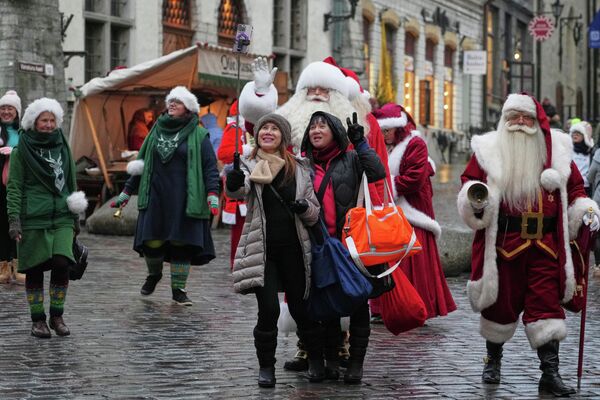 Туристы фотографируются с мужчинами в костюмах Санта-Клауса в Таллине  - Sputnik Латвия