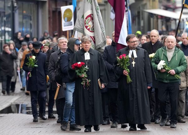 Люди идут по центру Риги с флагами, цветами, плакатами и эмблемами латышского легиона СС. - Sputnik Латвия