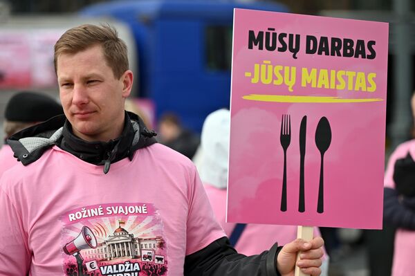 На фото: участник акции протеста держит плакат с надписью: "Наша работа — ваша пища". - Sputnik Латвия