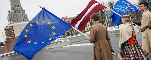 Юноша и девушка в национальных латышских костюмах с флагами ЕС и Латвии у Памятника Свободы в Риге - Sputnik Латвия