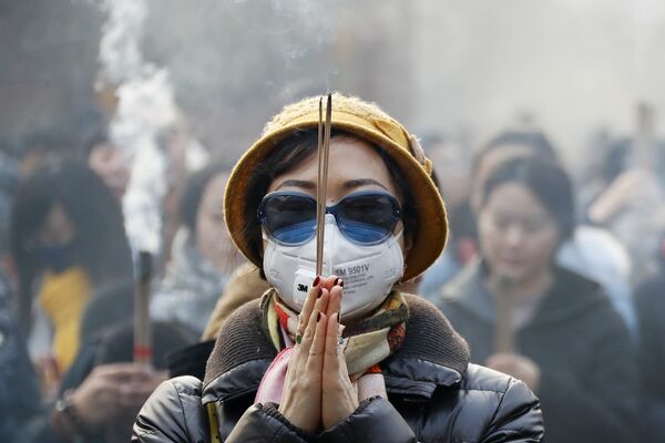 Женщина в маске и солнцезащитных очках во время молитвы в первый день Нового года в Пекине. - Sputnik Латвия