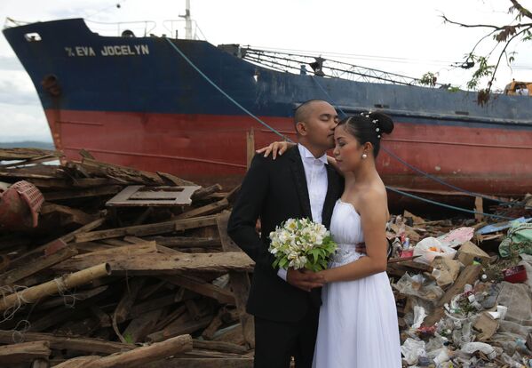 Жених Эрвин Нирва целует свою невесту Ризу на фоне разрушенных тайфуном домов и корабля на Филиппинах - Sputnik Латвия