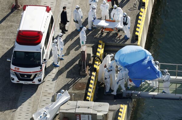 Сотрудники полиции в защитных костюмах помещают в машину скорой помощи заболевшего пассажира круизного лайнера Diamond Princes, помещенного в карантин у японского порта Йокогама - Sputnik Латвия